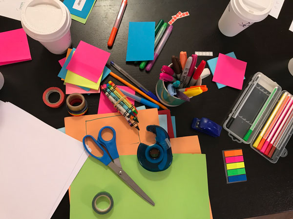 Messy desk with paper, scissors, crayons, markers, tape and more.