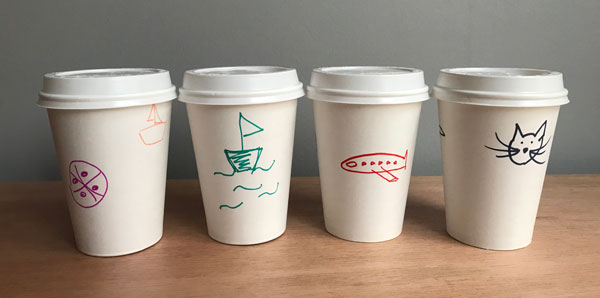 Blank to-go cups with drawings by participants: boats, cats, airplane.