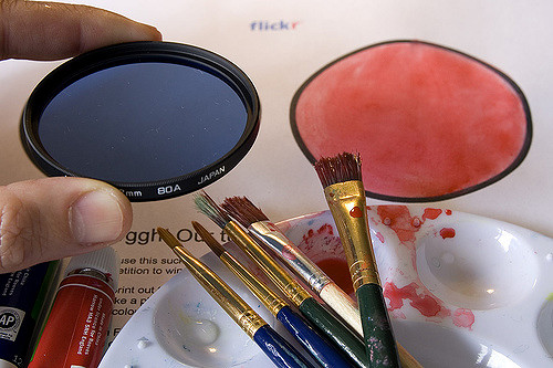 Printed coloring competition document with art supplies and a blue lens to create the logo of two circles: blue and pink.