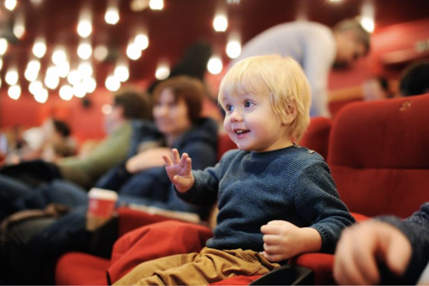 Un enfant sur un grand siège rouge d'une salle de spectacle