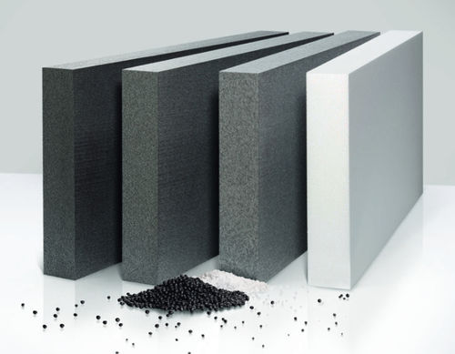 Panneaux isolants en polystyrène expansé (EPS) de différentes épaisseurs, principalement en teintes grises et blanches. À l’avant, des granulés noirs et blancs, utilisés pour la fabrication de ces panneaux, sont dispersés sur une surface blanche